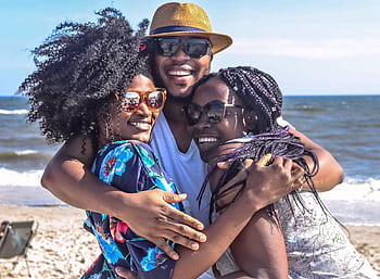 Three friends enjoying a sunny day at the beach, embracing with smiles. HD wallpaper