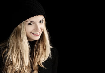 Beautiful woman with long blonde hair smiling in a black beanie against a dark background. HD wallpaper