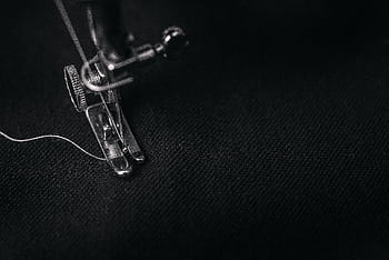 Detailed view of a sewing machine needle stitching fabric, highlighting sewing process and textile technology. HD wallpaper