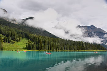 Canoeing on a pristine turquoise lake surrounded by misty mountains and pine forests, capturing a tranquil summer day. HD wallpaper