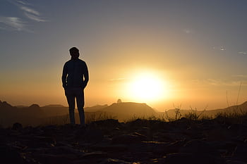 A lone silhouette of a man stands against a breathtaking sunset in the Amguel desert, Tamanrasset Province, Algeria. HD wallpaper
