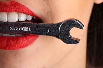 A close-up shot of red lips holding a shiny wrench with bold red lipstick. HD wallpaper