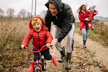 Father helping son ride a bicycle on a fall day while mother and daughter watch. HD wallpaper