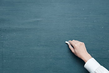 Hand holding chalk ready to write on a blank blackboard surface. HD wallpaper