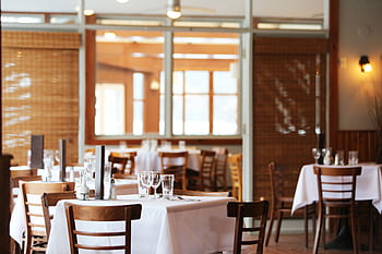 A serene restaurant interior with wooden chairs and tables set with glasses, ready for dining. HD wallpaper