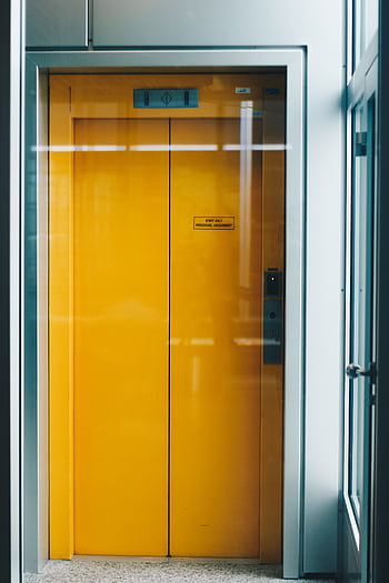 A bold yellow elevator door captured indoors, offering a bright contrast in modern architecture. HD phone wallpaper