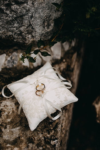 Close-up of wedding rings on a silky white cushion outdoors, captured in soft light. HD phone wallpaper