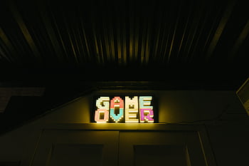 Glowing neon sign with pixelated Game Over text in a dark arcade setting. HD wallpaper