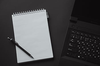 Flat lay of an office workspace with a laptop, notepad, and mechanical pencil on a black background. HD wallpaper