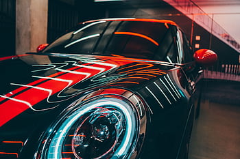 A luxury sports car in a modern setting with vibrant red and neon lights reflecting on the surface. HD wallpaper