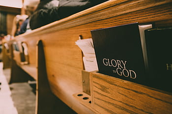 A close-up of a wooden church pew holding hymnals and a Bible, symbolizing worship. HD wallpaper