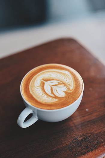 A beautifully crafted latte with intricate latte art inside a white ceramic cup on a wooden table. HD phone wallpaper