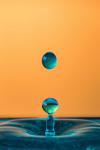 Mesmerizing close-up of turquoise water droplets against a striking orange background, showcasing liquid symmetry. HD phone wallpaper