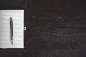 A minimalist open notebook with a pen on a dark wooden desk offering ample copyspace. HD wallpaper