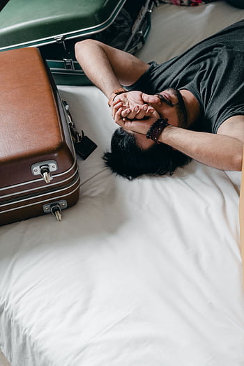 A young man rests on a bed, surrounded by luggage, reflecting a travel or moving theme. HD phone wallpaper