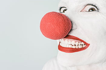 Bright close-up of a clown's face with red nose and makeup, showcasing humor and joy. HD wallpaper