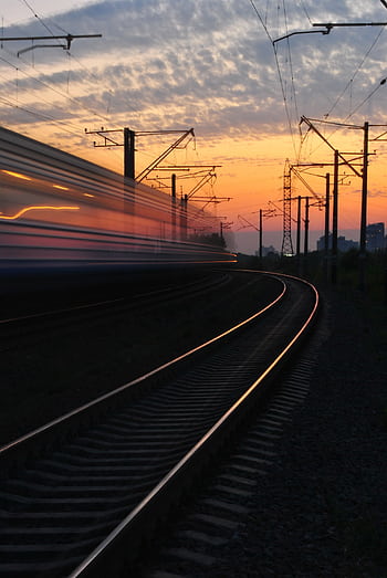 A dynamic shot capturing a blurred train speeding on curved tracks during a vibrant sunset. HD phone wallpaper