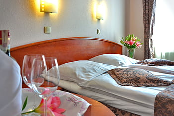Elegant hotel room featuring a cozy bed, wine glasses, and floral decor, creating a welcoming atmosphere. HD wallpaper