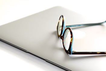 Close-up of eyeglasses on a sleek, modern laptop, ideal for office or remote work settings. HD wallpaper