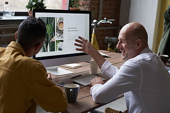 Two professionals collaborating in a modern workspace, discussing a project on a computer screen. HD wallpaper