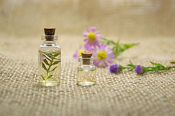 Glass bottles with essential oils and fresh flowers on burlap fabric creating a natural aroma. HD wallpaper
