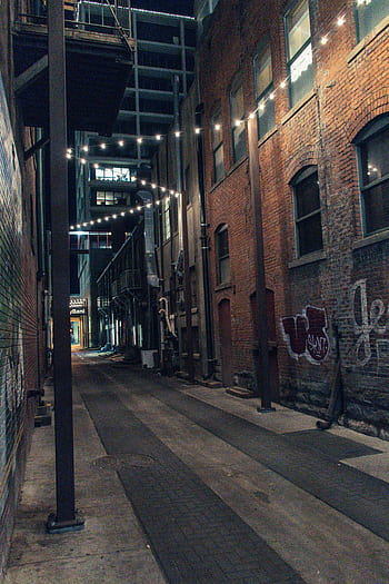 Cozy urban alley illuminated by string lights, showcasing brick architecture and a quiet ambiance at night. HD phone wallpaper