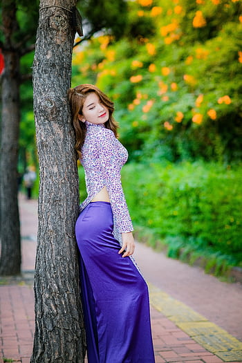 Stylish woman in a purple dress leaning on a tree with bright foliage. Perfect for editorial fashion. HD phone wallpaper