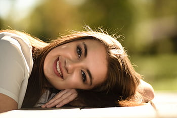 A young woman with long hair and a radiant smile lies on the grass during a sunny day. HD wallpaper