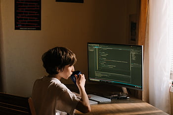 A young person coding at a desk with a computer and drinking from a mug. HD wallpaper