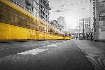 Dynamic long exposure of a yellow tram moving through urban streets, showcasing motion blur and city life. HD wallpaper