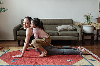 A joyful mother practicing yoga with her daughter on a colorful rug indoors. HD wallpaper