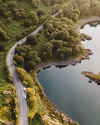 Aerial view of a winding road by a serene lake surrounded by lush greenery. HD phone wallpaper