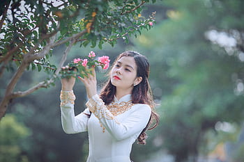 An elegant woman in traditional Ao Dai appreciating the beauty of pink blossoms. HD wallpaper