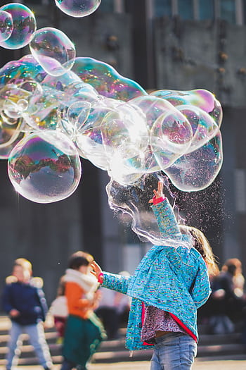 A child delights in chasing and popping giant bubbles in an outdoor setting. HD phone wallpaper