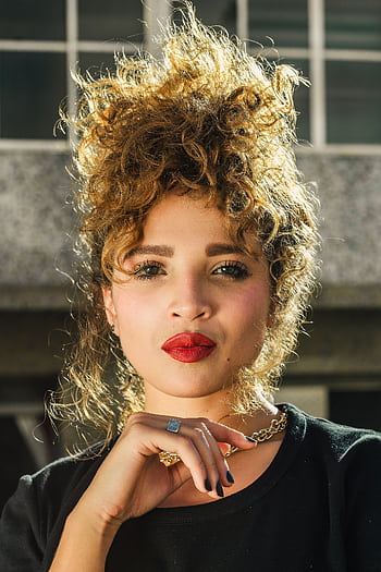 Portrait of a young woman with curly hair and red lips wearing a necklace outdoors. HD phone wallpaper
