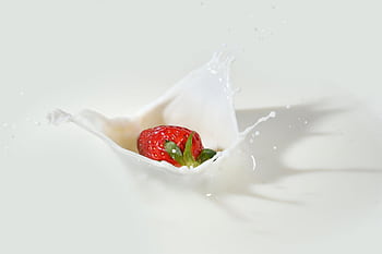 A vibrant strawberry makes a splash in creamy white milk, showcasing freshness and vivid colors. HD wallpaper