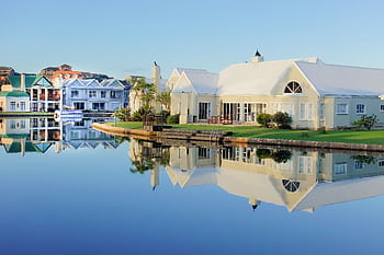 Serene view of elegant waterfront villas with perfect reflection on calm water. HD wallpaper