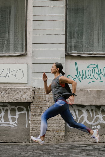 A woman in activewear jogging swiftly past a graffitied wall in an urban setting. HD phone wallpaper