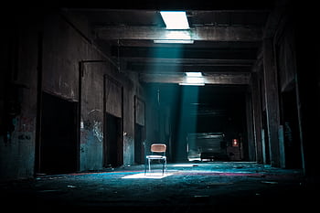 Eerie abandoned warehouse with a solitary chair illuminated by sunlight, evoking mystery. HD wallpaper