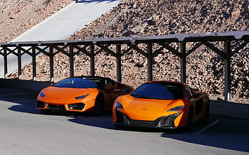 Two orange luxury sports cars parked under a wooden structure in Boulder City, Nevada. HD wallpaper