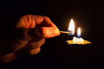 A hand uses a match to light a candle in a dimly lit environment. HD wallpaper