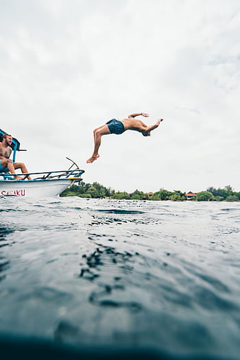 A man performs a backflip dive into the ocean from a boat, capturing a moment of adventure in Indonesia. HD phone wallpaper