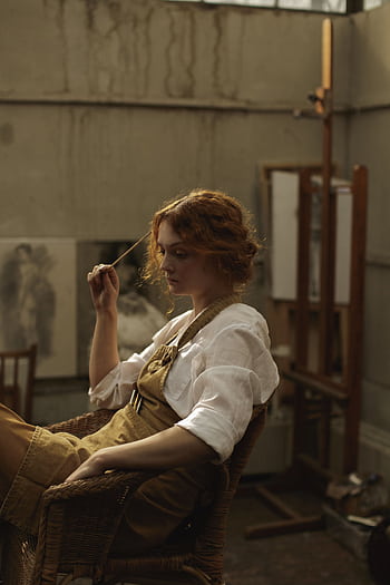 Young female artist in deep thought, sitting in a rustic studio. Shows creativity and contemplation. HD phone wallpaper