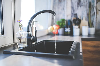 A modern kitchen sink with running water, a sleek faucet, and a vase on the countertop. HD wallpaper