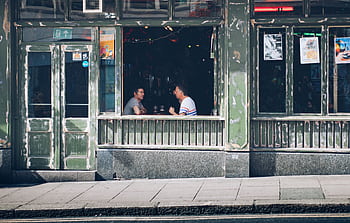 Two men enjoy a casual conversation inside a vintage-style café. HD wallpaper
