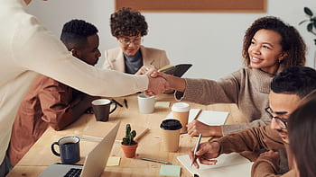 Colleagues collaborating indoors, sharing smiles, and shaking hands during a business meeting. HD wallpaper