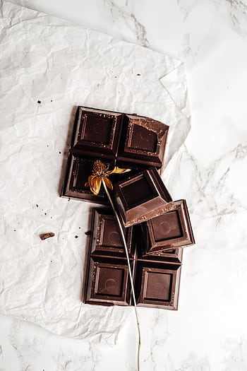 A flat lay of dark chocolate pieces with a dried flower elegantly placed, emphasizing artisanal confectionery. HD phone wallpaper