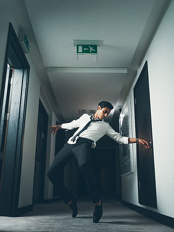 Stylish man striking a dance pose in a modern hallway with overhead lighting. HD phone wallpaper