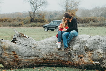 A couple embraces tenderly on a large fallen tree, set against a serene natural landscape. HD wallpaper