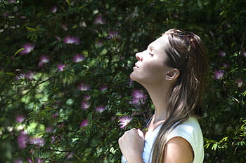 A woman enjoying a serene moment in a sunlit garden, surrounded by vibrant flowers. HD wallpaper